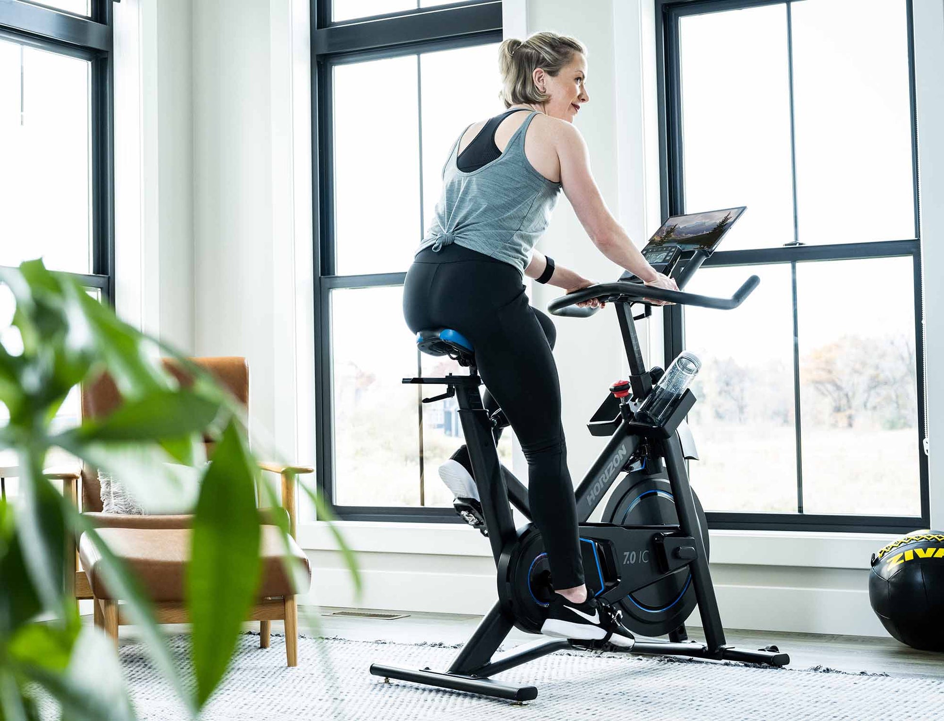 Woman exercising on a 5.0 stationary bike in a home setting with large windows.